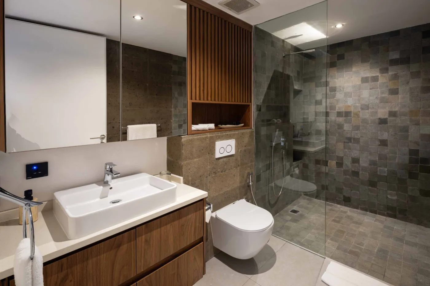 Modern minimalist bathroom with wooden slat walls, floating walnut vanity, white sink, large mirror, and adjacent open doorway. - Bali Villas