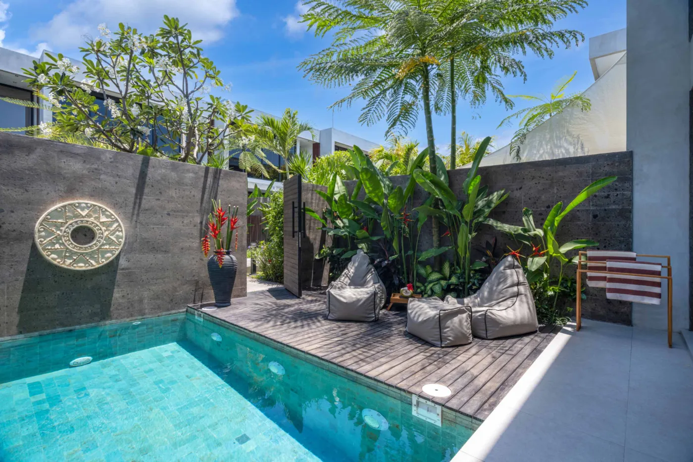 Serene private infinity pool in a tropical Bali villa, surrounded by lush palms, bean bag seating, and modern stone walls. - Bali Villas