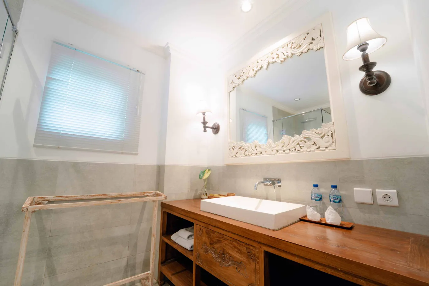 Modern bathroom featuring white toilet, glass shower enclosure, hanging towel, and wooden stool. - Bali Villas