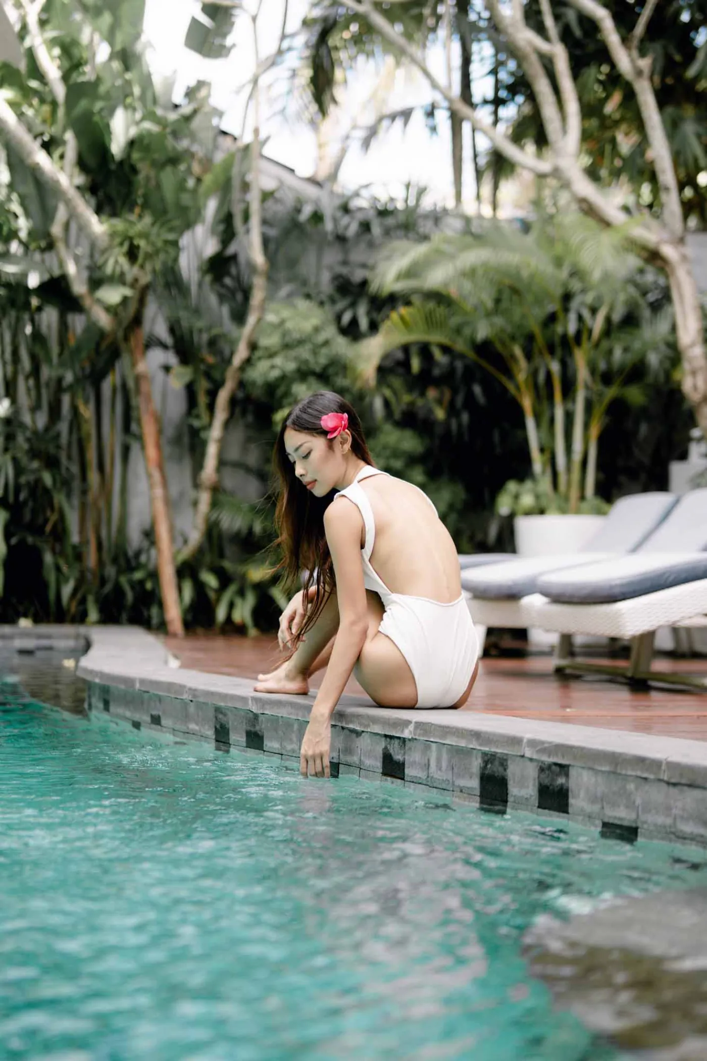Modern bathroom featuring white toilet, glass shower enclosure, hanging towel, and wooden stool. - Bali Villas