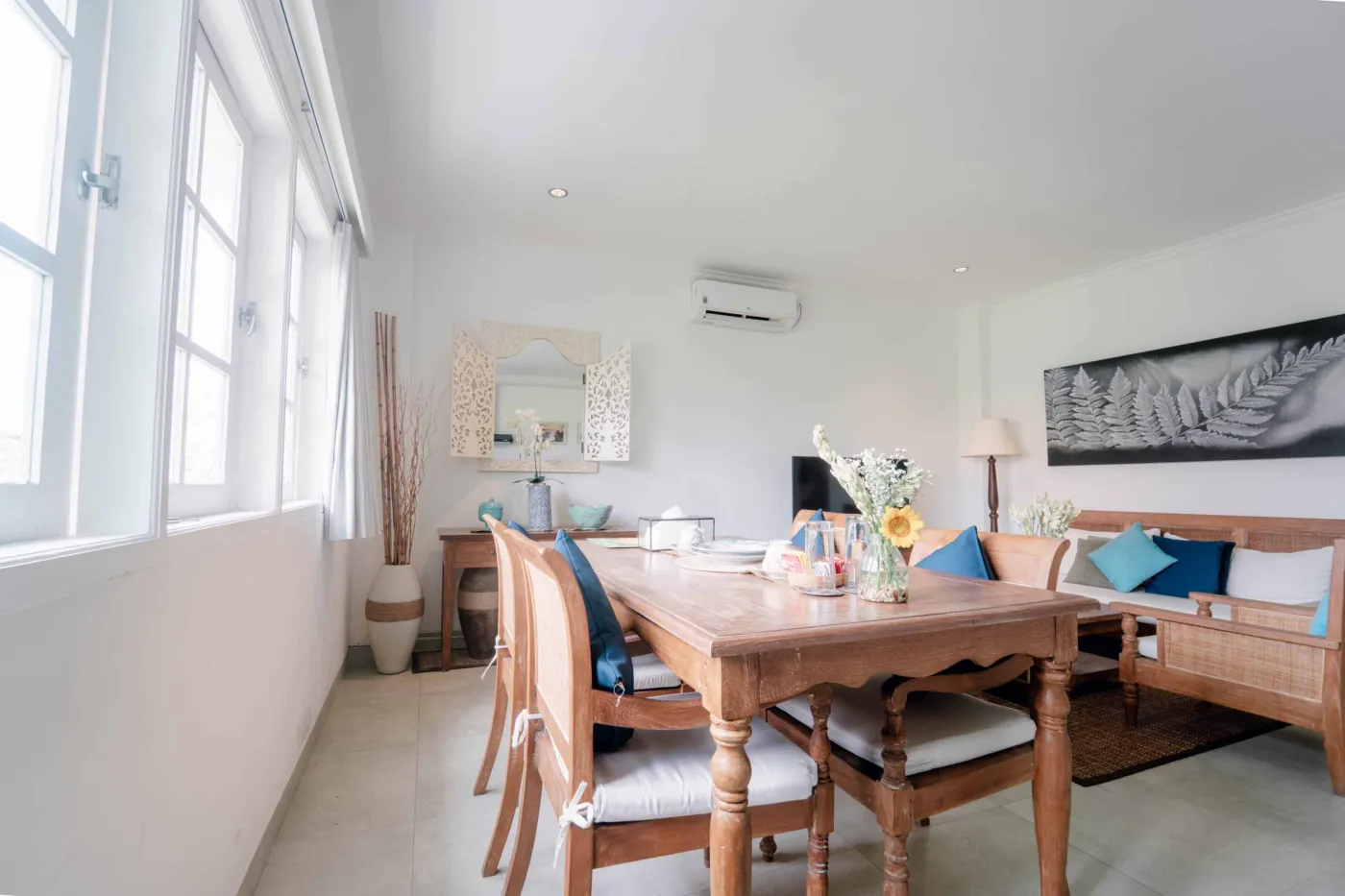 Spacious modern bathroom with wooden vanity, white sink, ornate carved mirror, towels, water bottles, and tropical decor. - Bali Villas