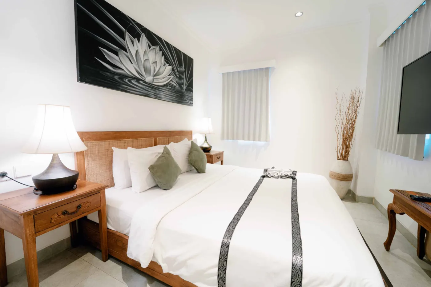 Modern bathroom with wooden vanity, white sink, ornate mirror, wall sconces, potted plant, toilet, and bottled water. - Bali Villas