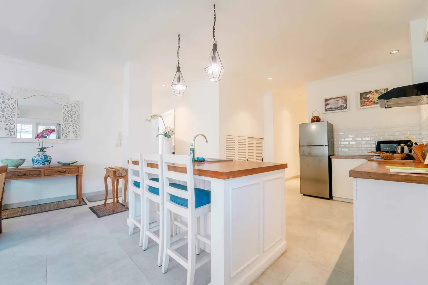 Modern bathroom interior with wooden vanity, white sink, ornate mirror, potted plant, and freestanding toilet. - Bali Villas