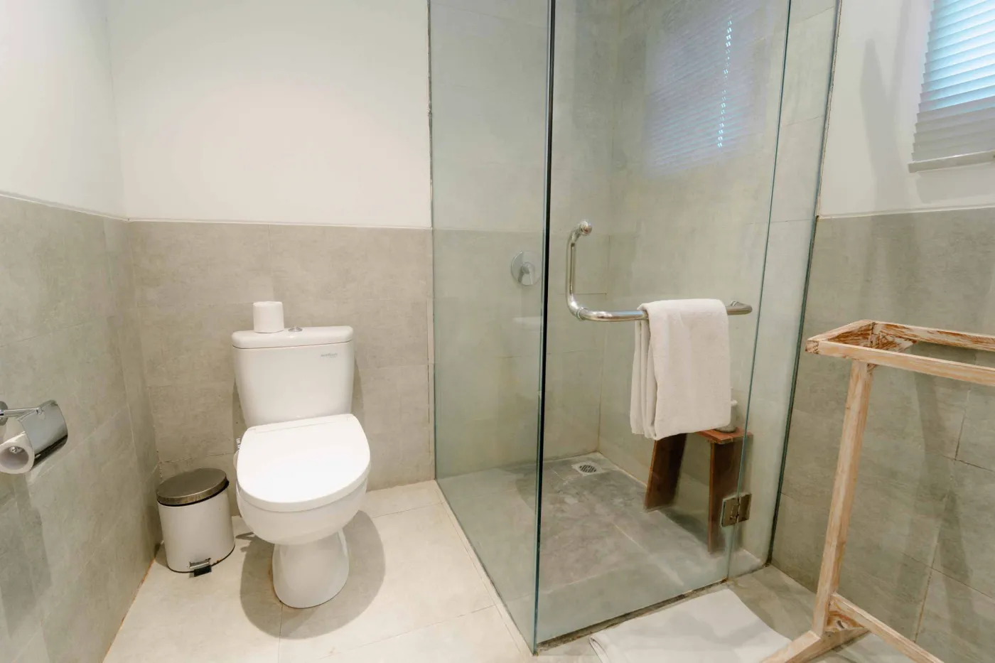 Modern white bathroom with toilet, glass shower, towel rail, and wastebasket. - Bali Villas