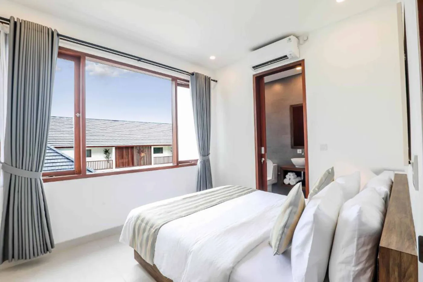 Modern Bali villa living room with beige sofas, glass dining table, Netflix on wall TV, potted plants, and sliding doors to infinity pool. - Bali Villas