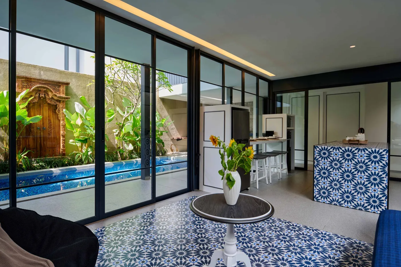 Modern minimalist bathroom with gray tiled walk-in shower, sleek black-framed vanity, pendant-lit round mirror, and potted plant. - Bali Villas