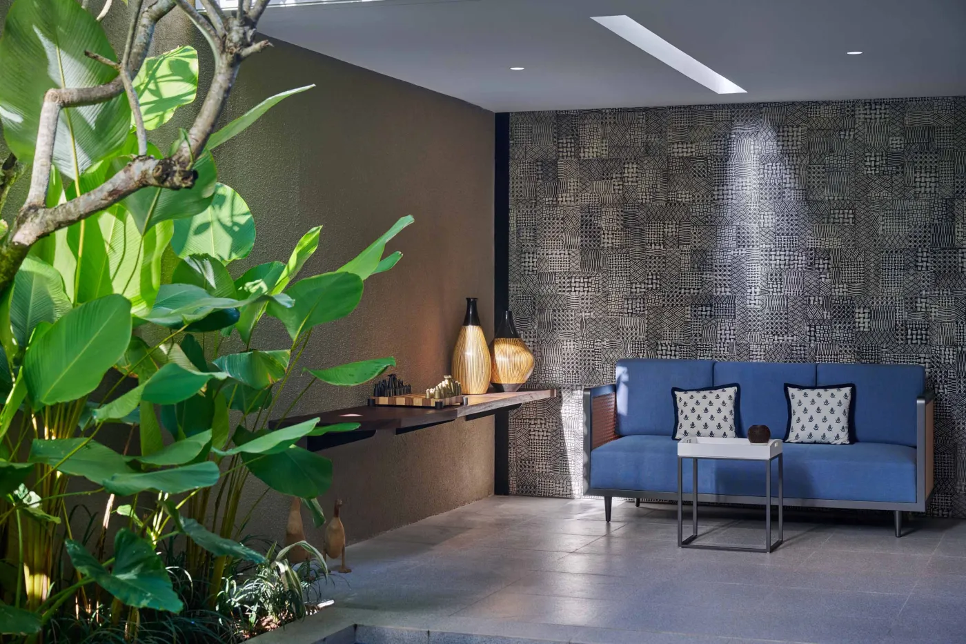 Modern minimalist bathroom with gray tiled walk-in shower, sleek black-framed vanity, pendant-lit round mirror, and potted plant. - Bali Villas