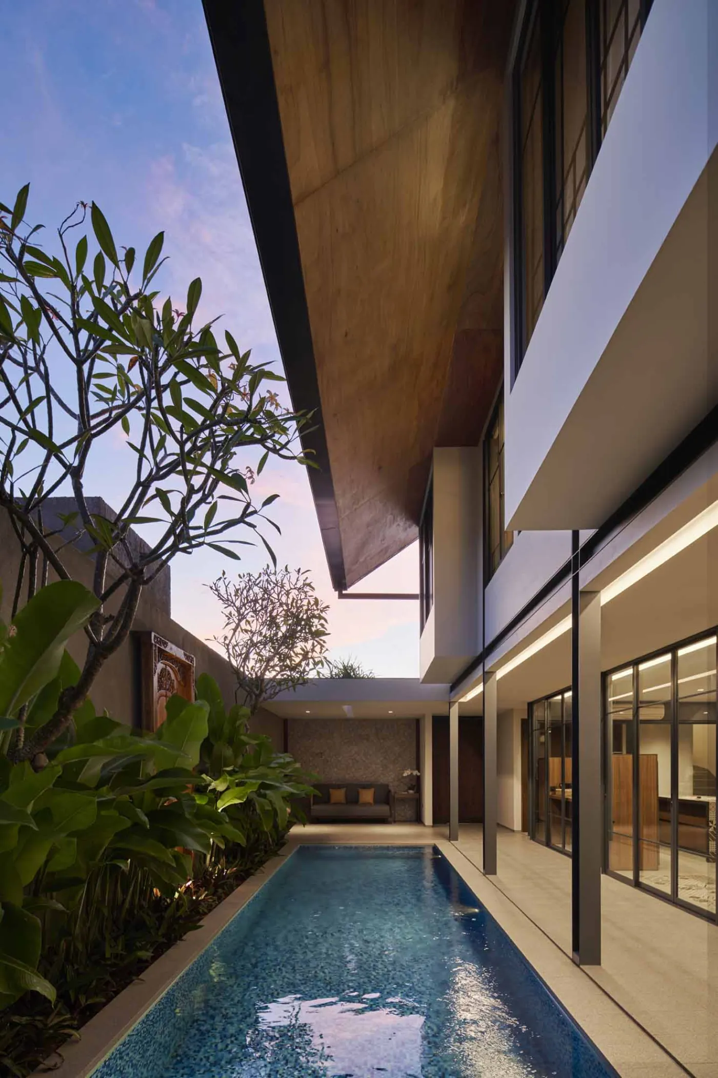 Modern minimalist bathroom with gray tiled walk-in shower, sleek black-framed vanity, pendant-lit round mirror, and potted plant. - Bali Villas