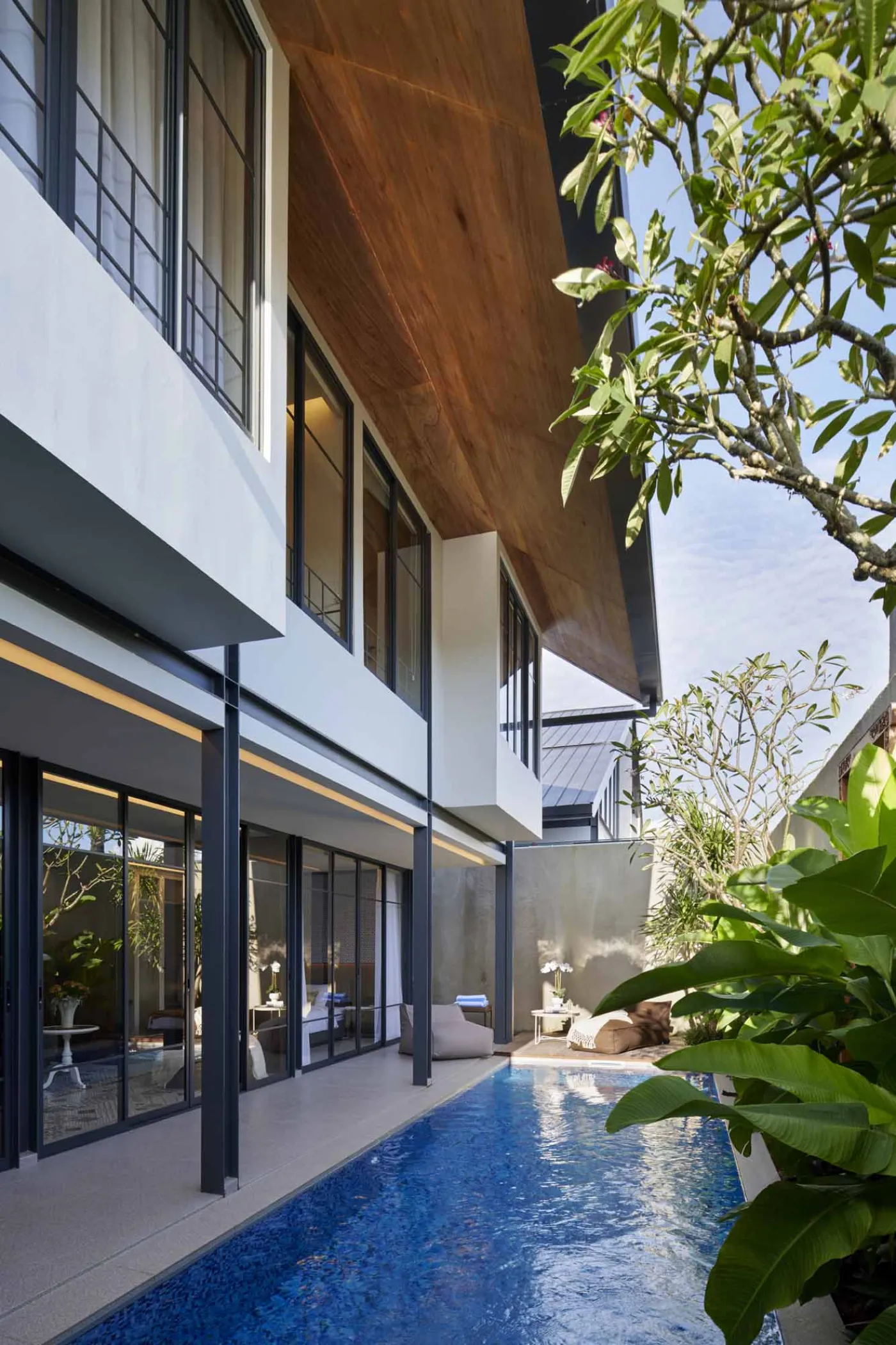 Modern minimalist bathroom with gray tiled walk-in shower, sleek black-framed vanity, pendant-lit round mirror, and potted plant. - Bali Villas