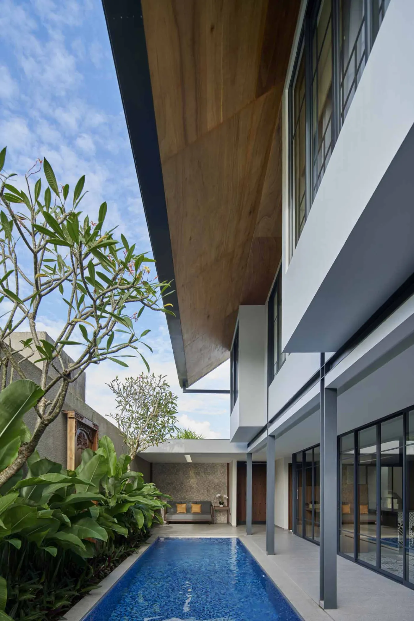 Modern minimalist bathroom with gray tiled walk-in shower, sleek black-framed vanity, pendant-lit round mirror, and potted plant. - Bali Villas