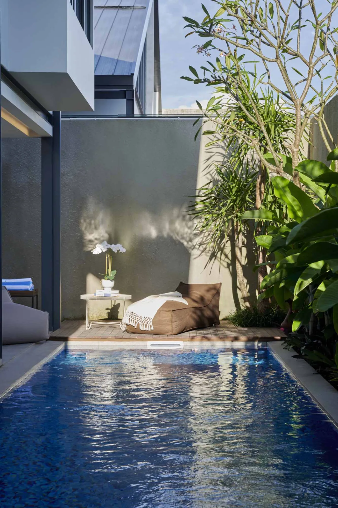 Modern minimalist bathroom with gray tiled walk-in shower, sleek black-framed vanity, pendant-lit round mirror, and potted plant. - Bali Villas