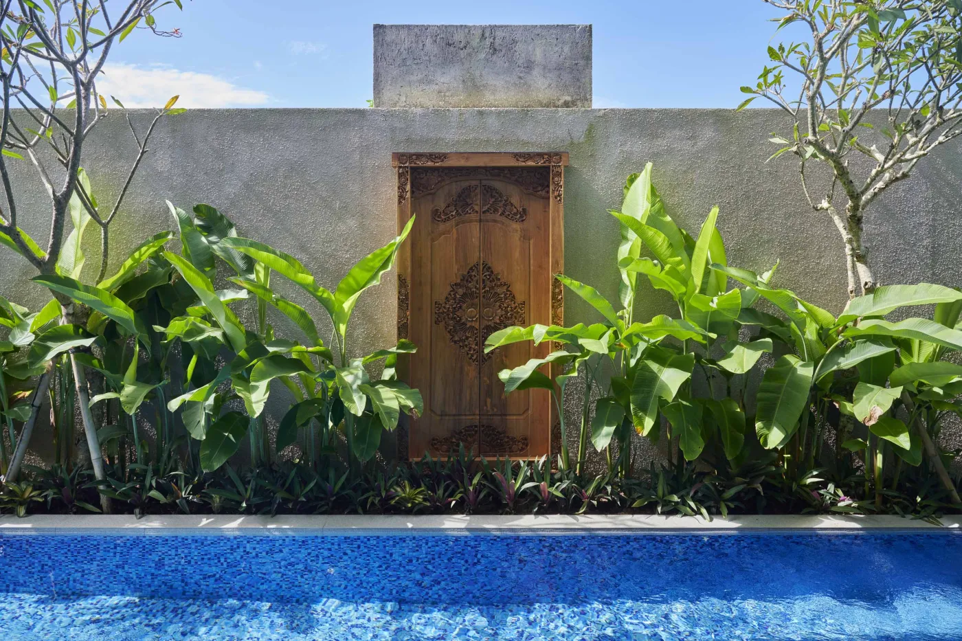 Modern minimalist bathroom with gray tiled walk-in shower, sleek black-framed vanity, pendant-lit round mirror, and potted plant. - Bali Villas