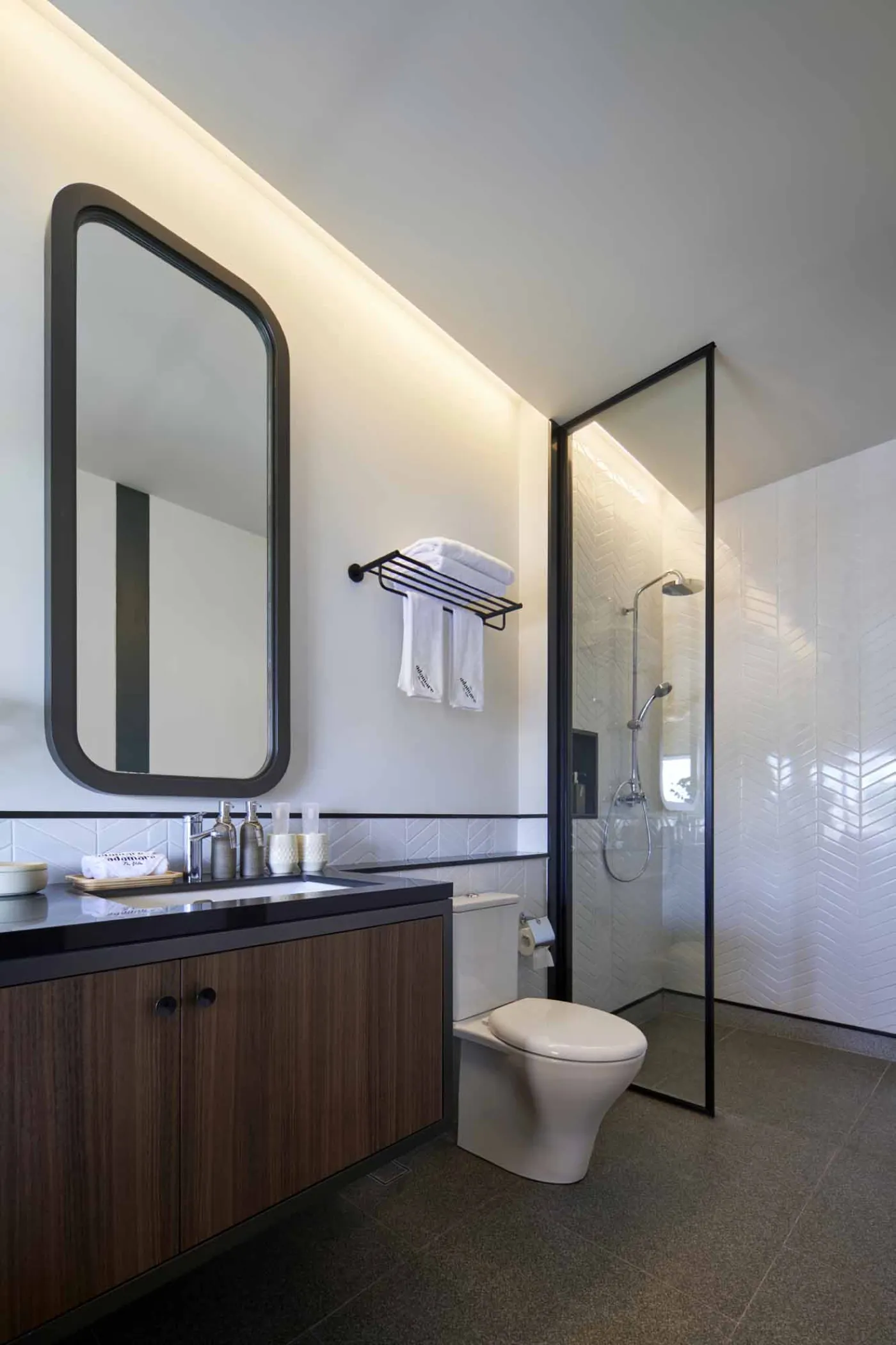 Modern minimalist bathroom with gray tiled walk-in shower, sleek black-framed vanity, pendant-lit round mirror, and potted plant. - Bali Villas