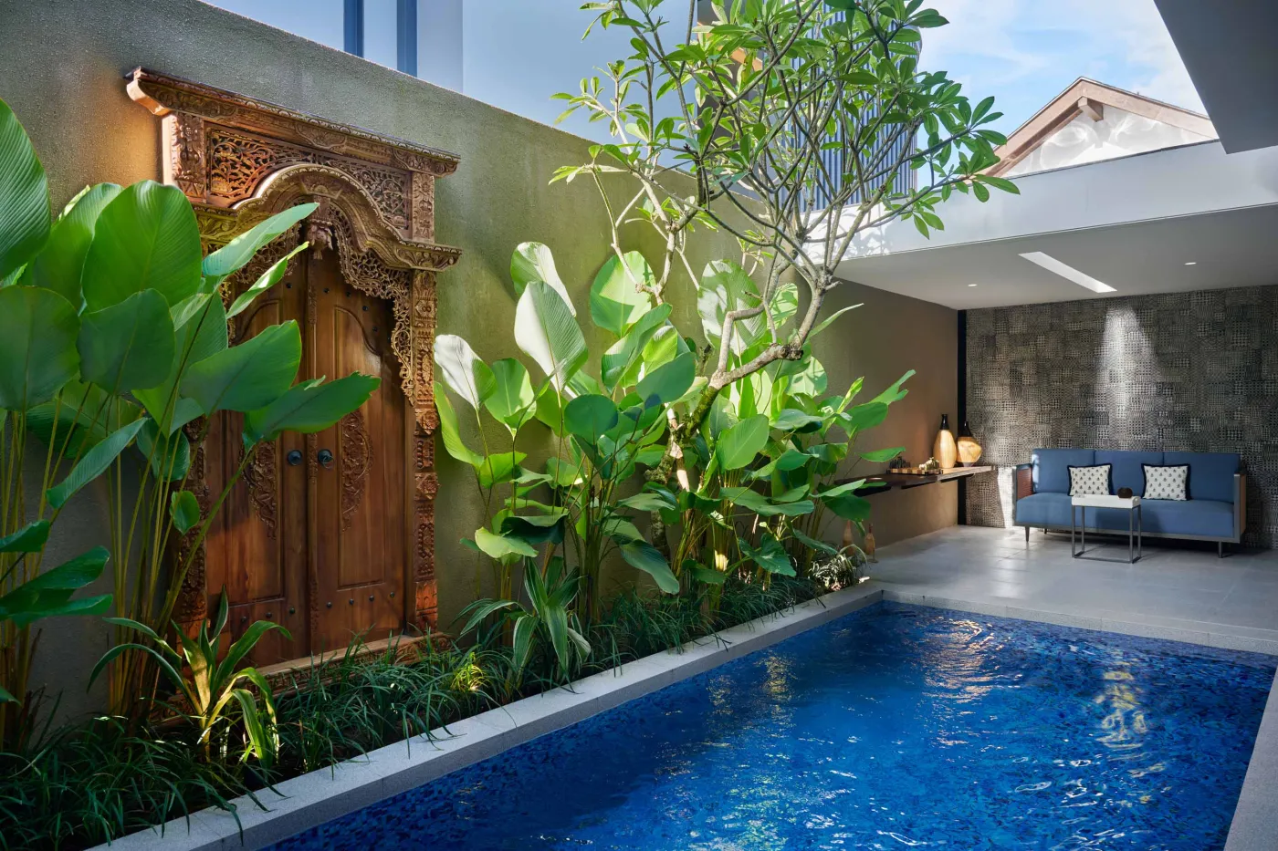 Modern minimalist bathroom with gray tiled walk-in shower, sleek black-framed vanity, pendant-lit round mirror, and potted plant. - Bali Villas