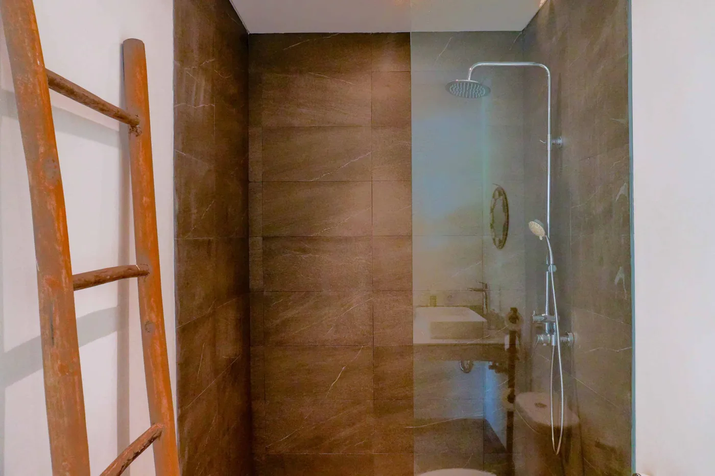 Minimalist modern bathroom with open wooden French door, wall-mounted white sink, round mirror, wooden towel rack, and corner toilet. - Bali Villas