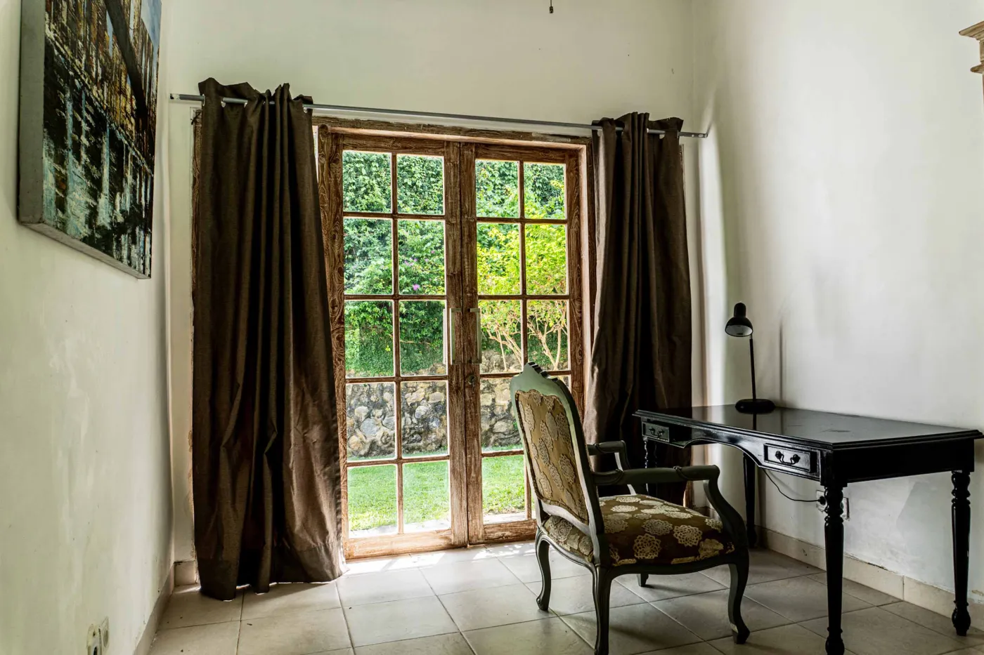 Minimalist modern bathroom with open wooden French door, wall-mounted white sink, round mirror, wooden towel rack, and corner toilet. - Bali Villas