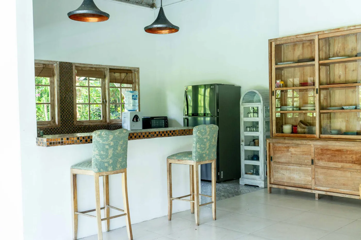 Minimalist modern bathroom with open wooden French door, wall-mounted white sink, round mirror, wooden towel rack, and corner toilet. - Bali Villas