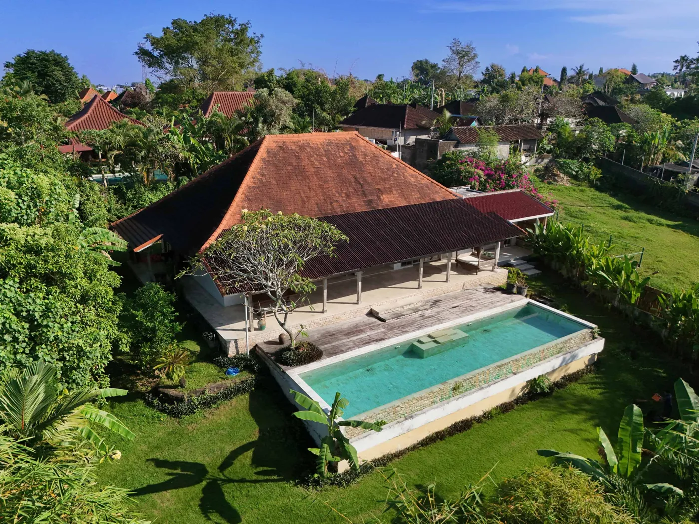 Spacious tropical villa interior with open wooden architecture, modern kitchen, cozy seating area, and lush garden view. - Bali Villas