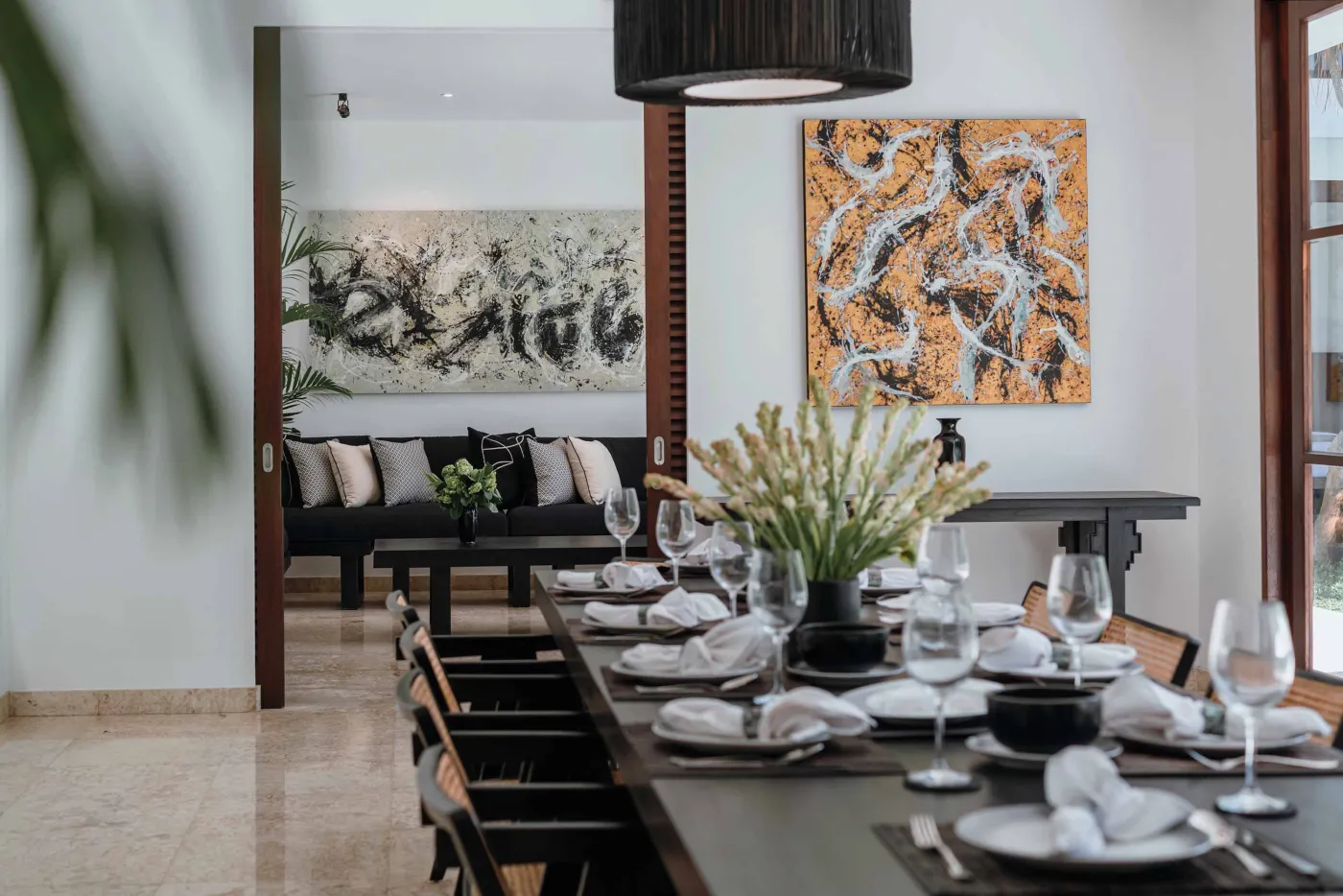 Modern tropical kitchen with white cabinets, granite island topped with fresh fruits, black appliances, and views of lush greenery. - Bali Villas