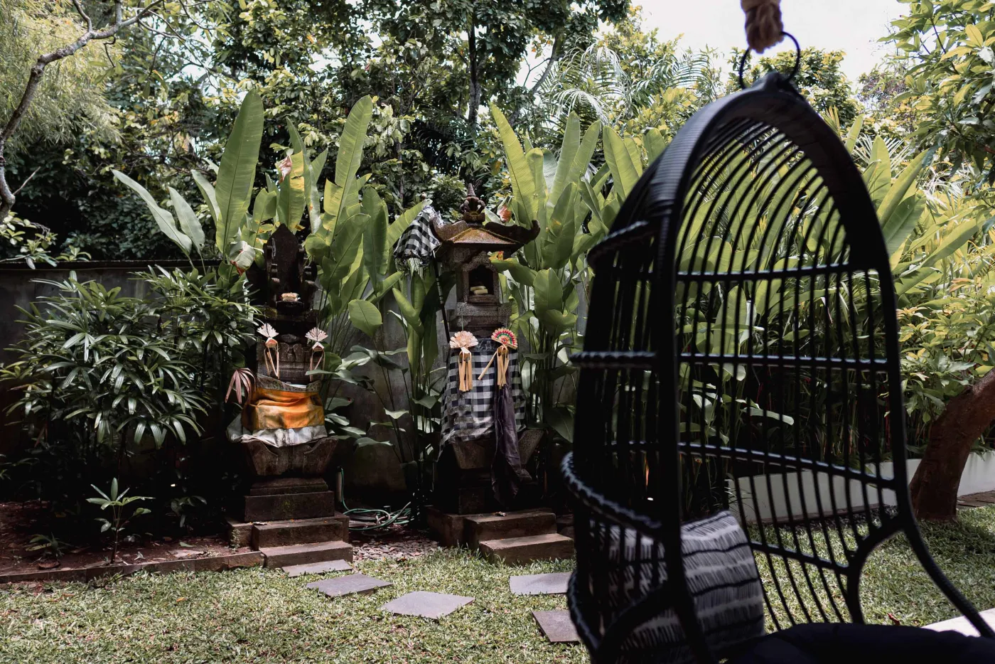 Modern tropical kitchen with white cabinets, granite island topped with fresh fruits, black appliances, and views of lush greenery. - Bali Villas