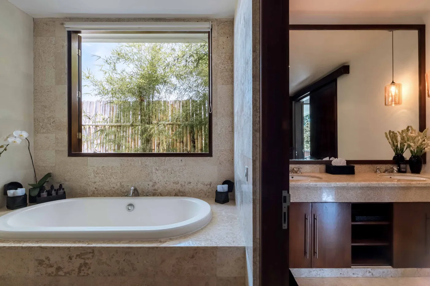 Modern tropical kitchen with white cabinets, granite island topped with fresh fruits, black appliances, and views of lush greenery. - Bali Villas