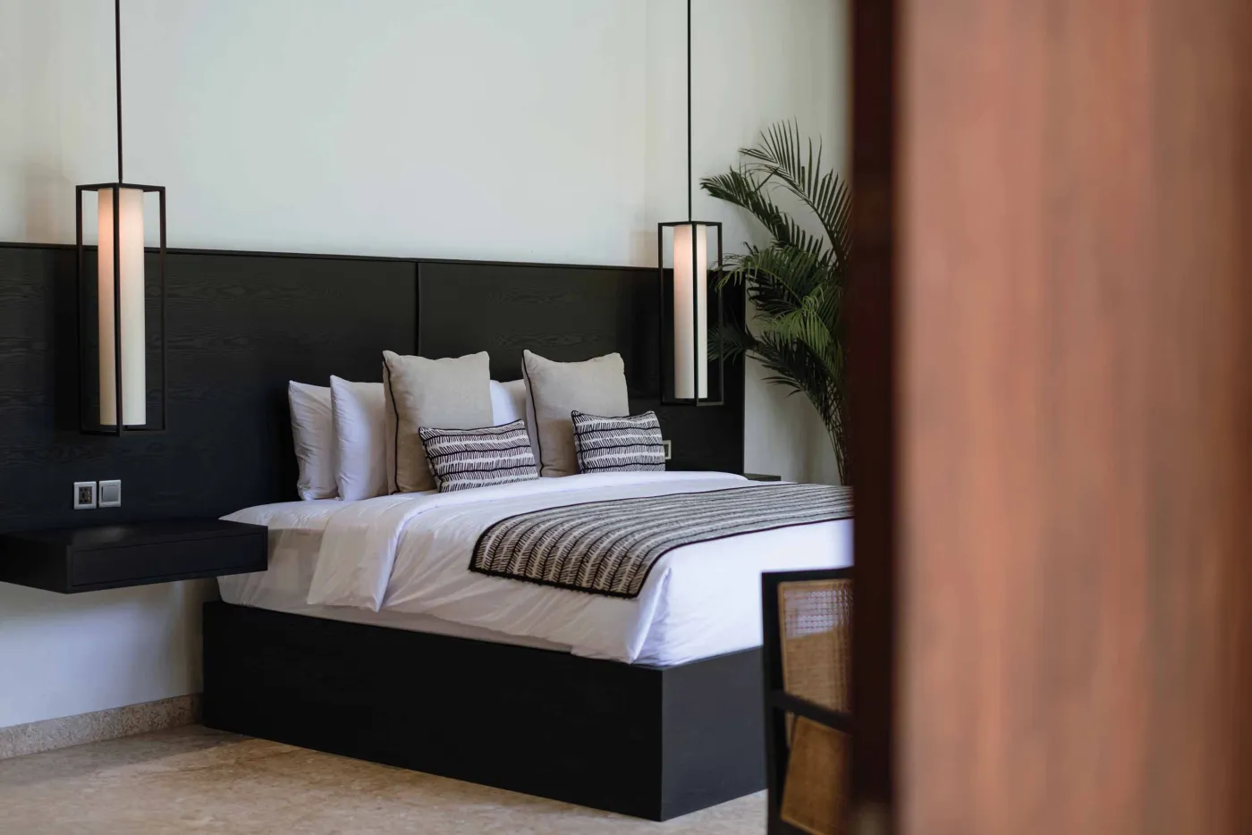 Modern tropical kitchen with white cabinets, granite island topped with fresh fruits, black appliances, and views of lush greenery. - Bali Villas