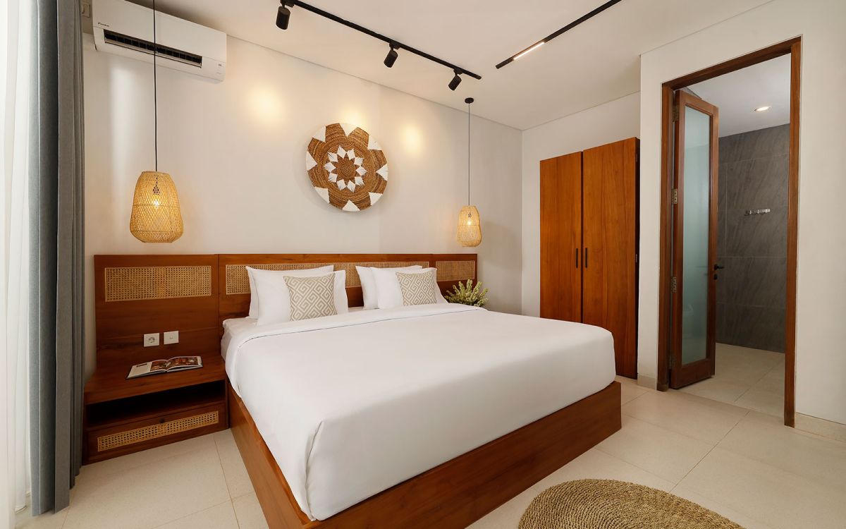 Spacious modern tropical bedroom with wooden bed, desk, mirror, and woven wall hangings under warm pendant lights. - Bali Villas
