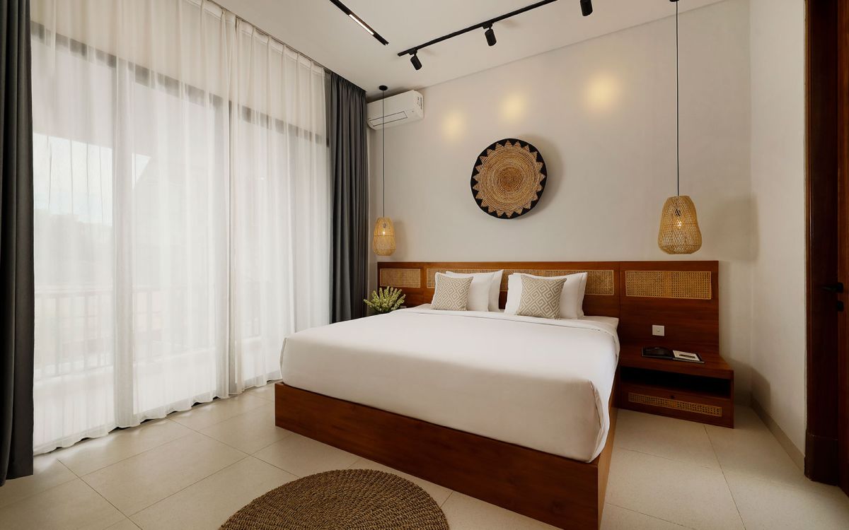 Spacious modern tropical bedroom with wooden bed, desk, mirror, and woven wall hangings under warm pendant lights. - Bali Villas
