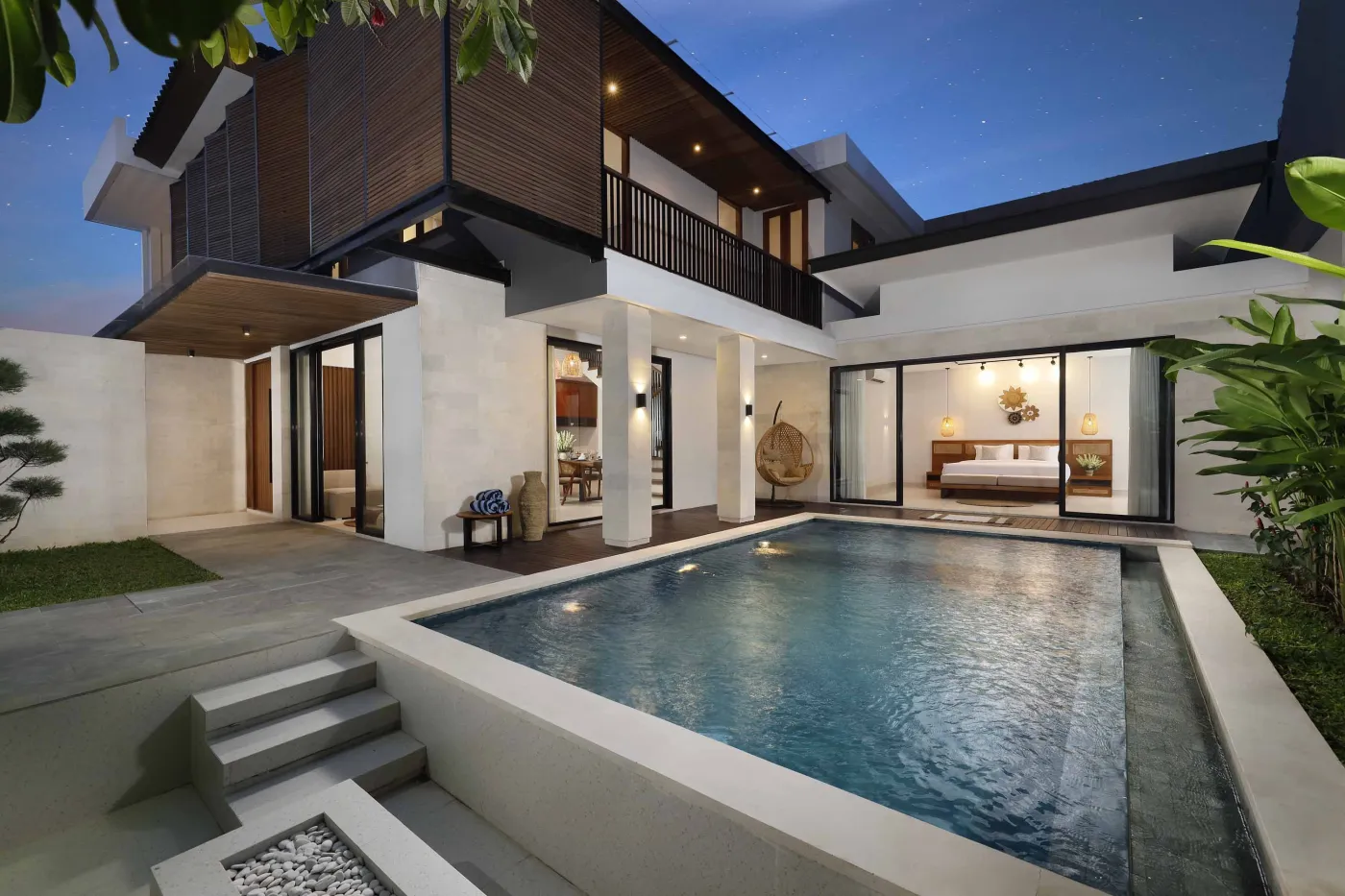 Modern tropical villa with infinity-edge pool, wooden accents, and lush greenery at dusk. - Bali Villas