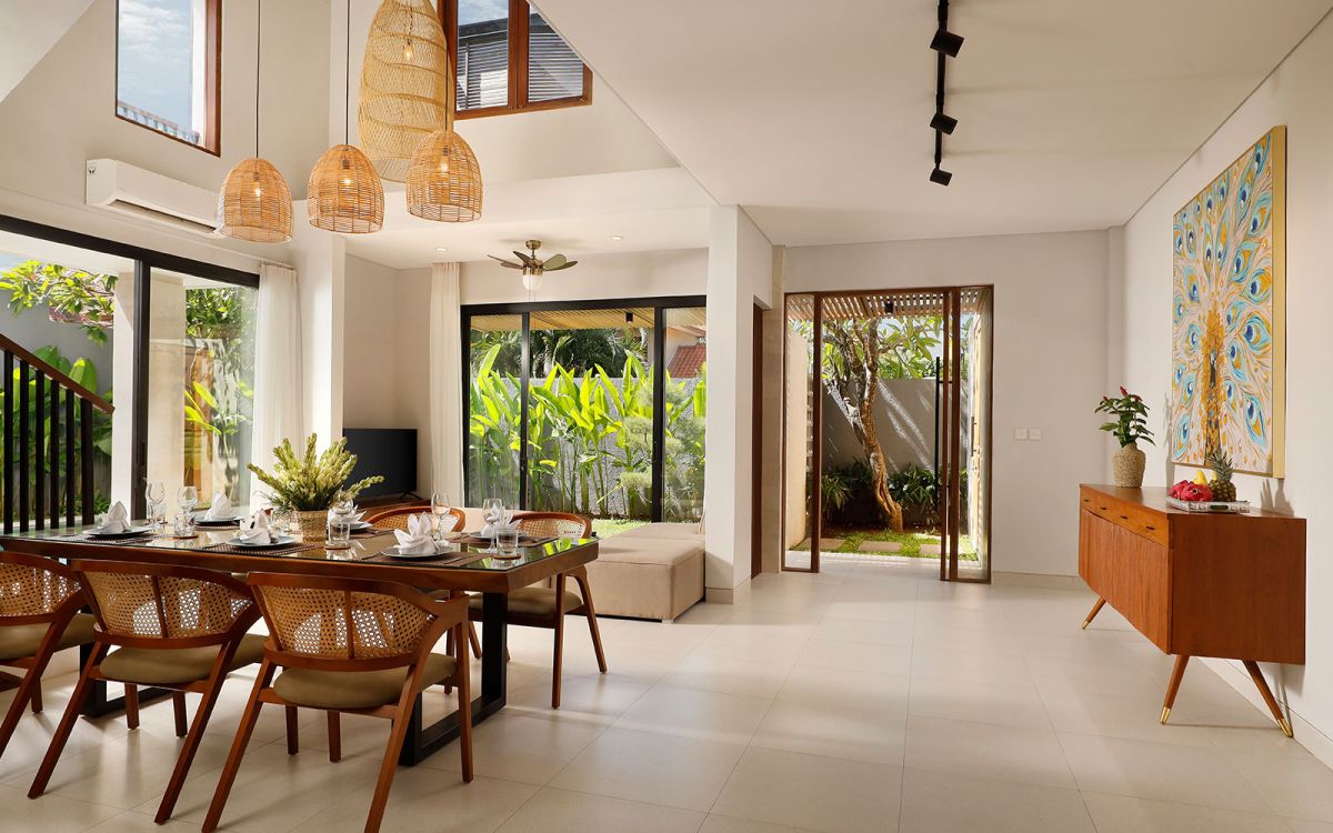 Spacious modern tropical bedroom with wooden bed, desk, mirror, and woven wall hangings under warm pendant lights. - Bali Villas