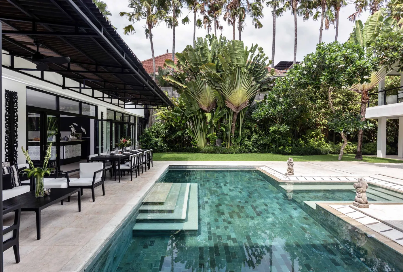 Well-stocked wooden wine cellar featuring diverse bottles of wine and spirits on shelves, with a small tasting table holding glasses and a red wine bottle. - Bali Villas