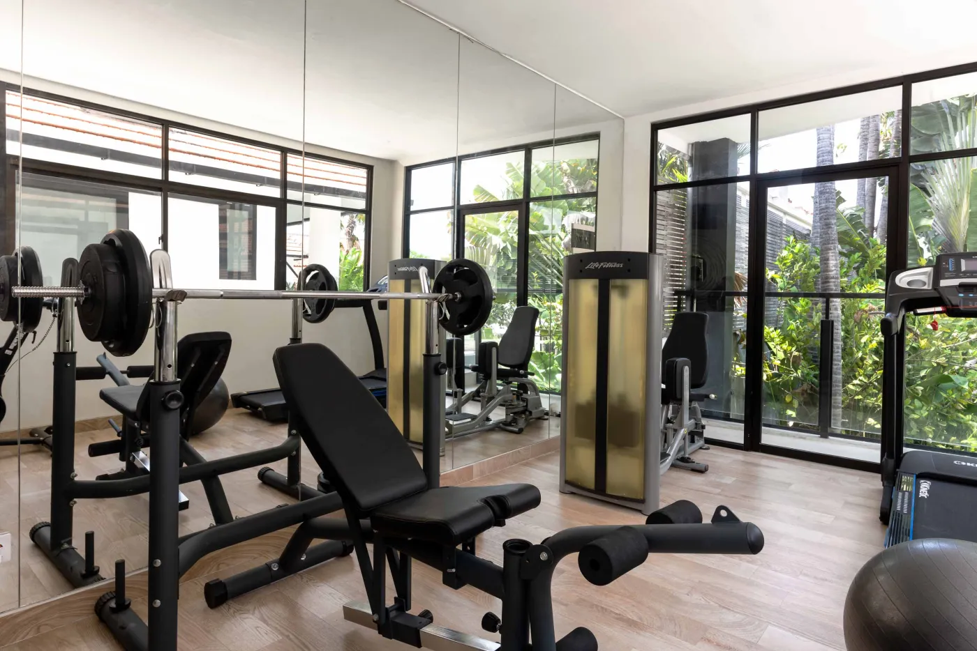 Well-stocked wooden wine cellar featuring diverse bottles of wine and spirits on shelves, with a small tasting table holding glasses and a red wine bottle. - Bali Villas