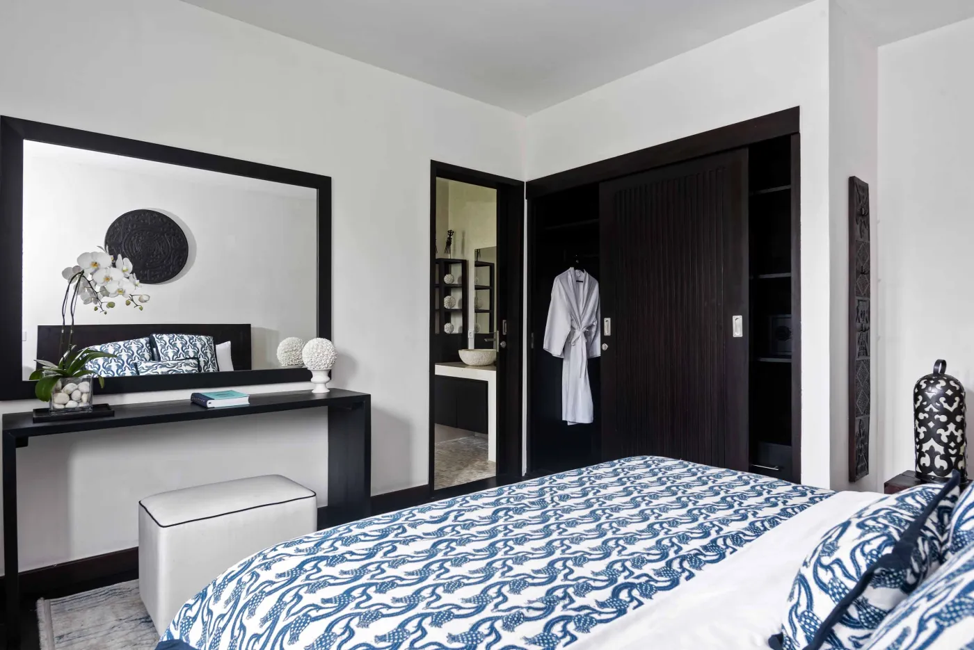 Well-stocked wooden wine cellar featuring diverse bottles of wine and spirits on shelves, with a small tasting table holding glasses and a red wine bottle. - Bali Villas