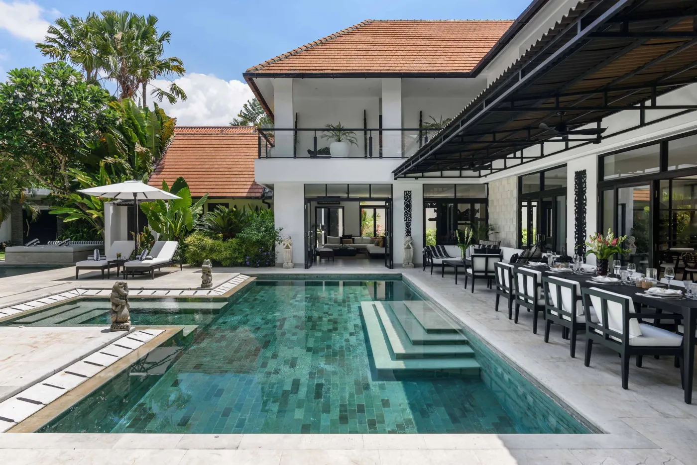 Luxurious modern Bali villa with infinity edge pool, outdoor dining terrace, and tropical gardens under sunny skies. - Bali Villas