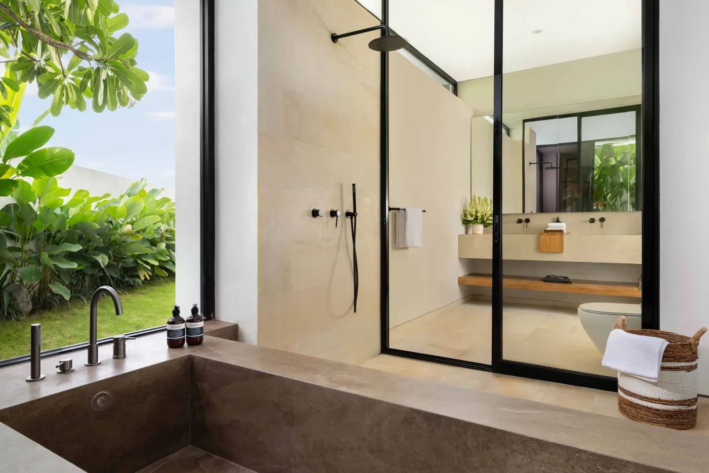 Modern luxury bathroom with freestanding bathtub, walk-in rain shower, wooden accents, and bedroom view. - Bali Villas
