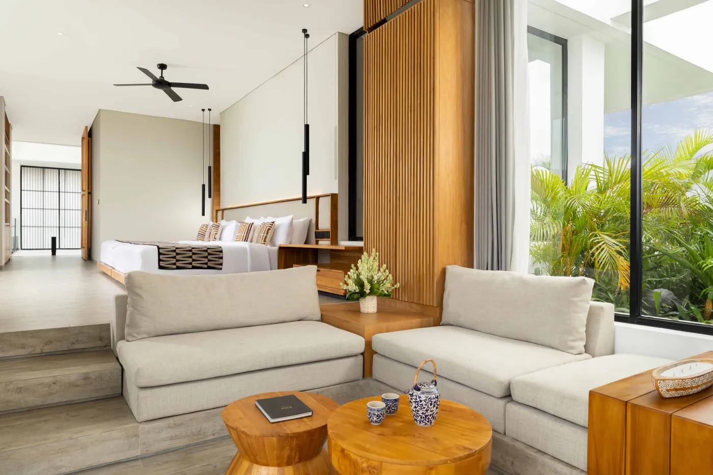 Modern luxury bathroom with freestanding bathtub, walk-in rain shower, wooden accents, and bedroom view. - Bali Villas