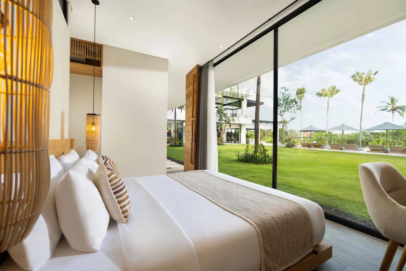 Modern luxury bathroom with freestanding bathtub, walk-in rain shower, wooden accents, and bedroom view. - Bali Villas