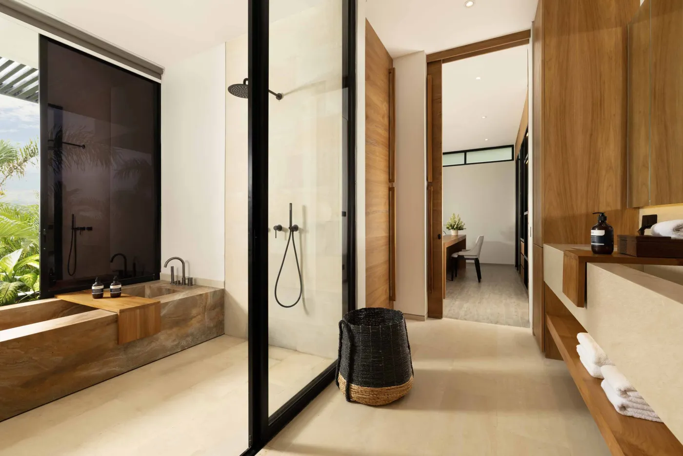 Modern luxury bathroom with freestanding bathtub, walk-in rain shower, wooden accents, and bedroom view. - Bali Villas