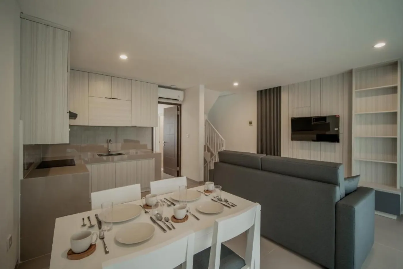 Modern white kitchen with sleek cabinets, induction cooktop, sink, microwave, and adjacent dining table with chairs. - Bali Villas