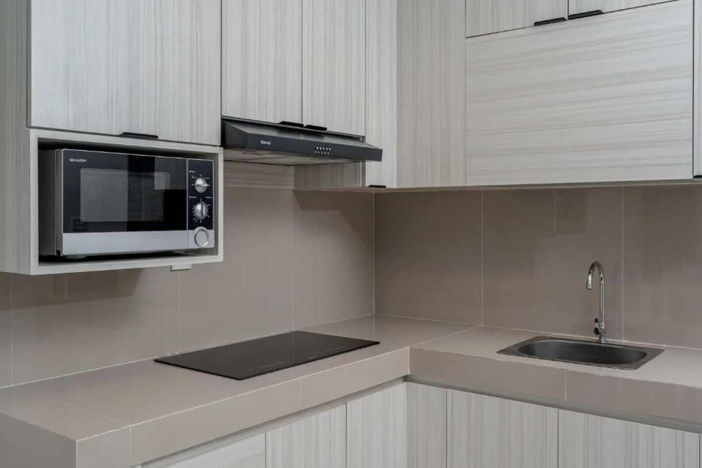 Modern white kitchen with sleek cabinets, induction cooktop, sink, microwave, and adjacent dining table with chairs. - Bali Villas