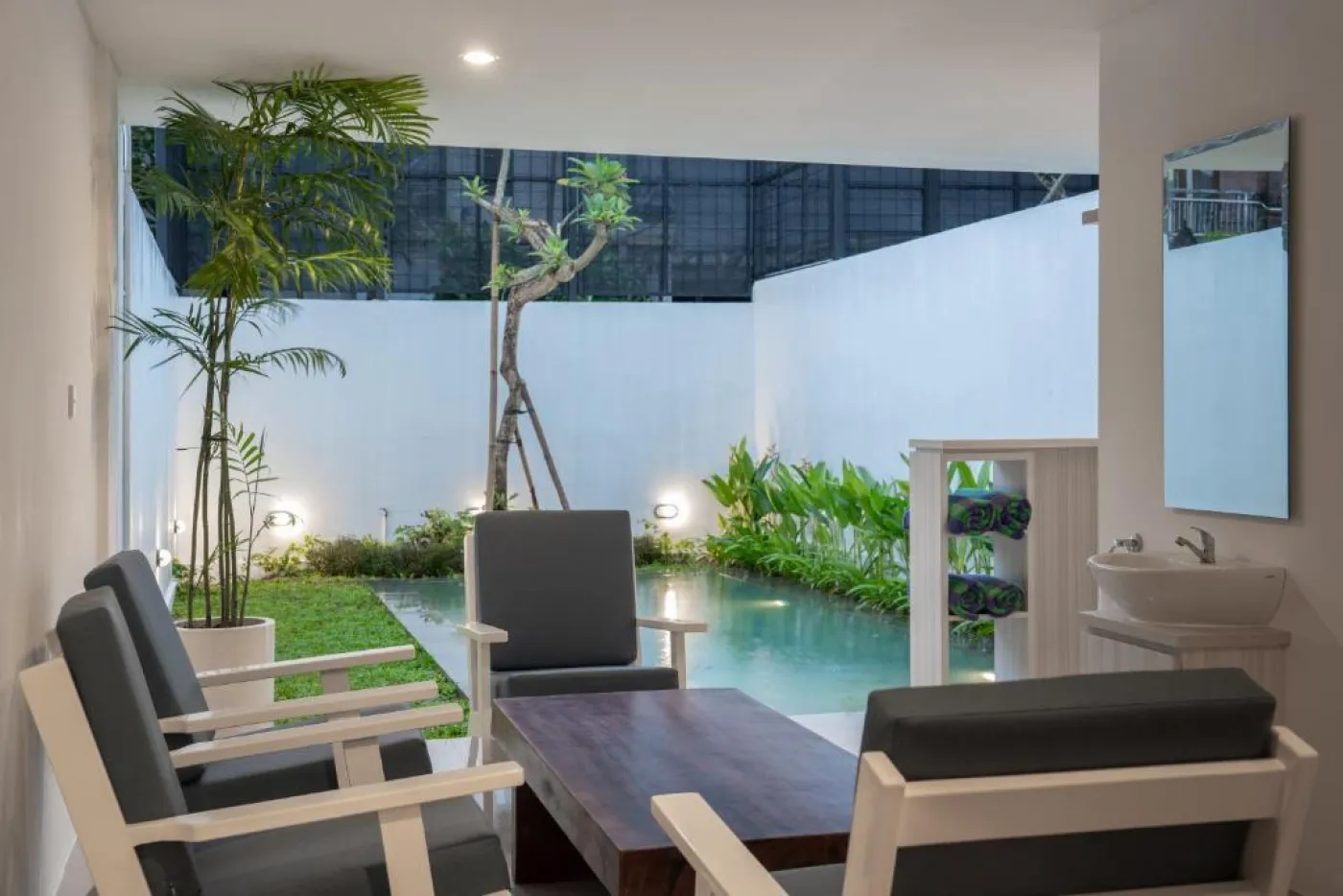 Modern white kitchen with sleek cabinets, induction cooktop, sink, microwave, and adjacent dining table with chairs. - Bali Villas
