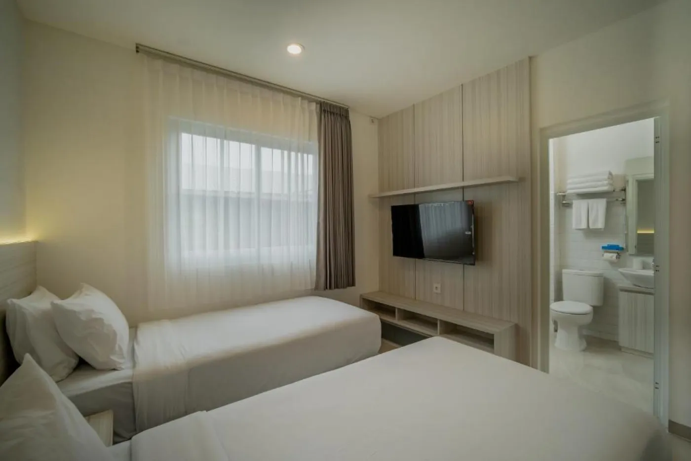 Modern minimalist living room interior with gray sofa, wooden coffee table, wall-mounted TV, built-in white shelves, and adjacent stairs. - Bali Villas