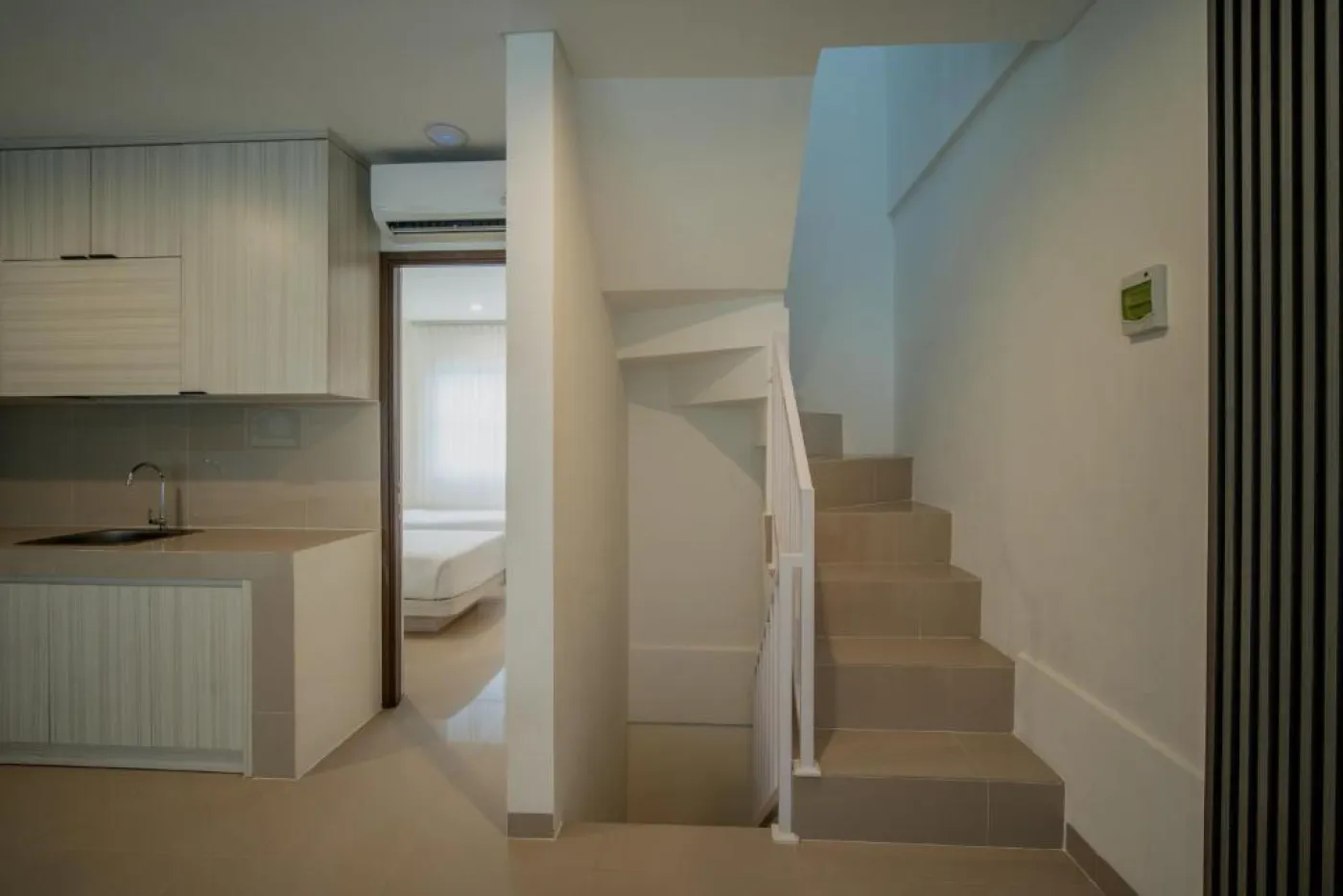 Modern minimalist living room interior with gray sofa, wooden coffee table, wall-mounted TV, built-in white shelves, and adjacent stairs. - Bali Villas