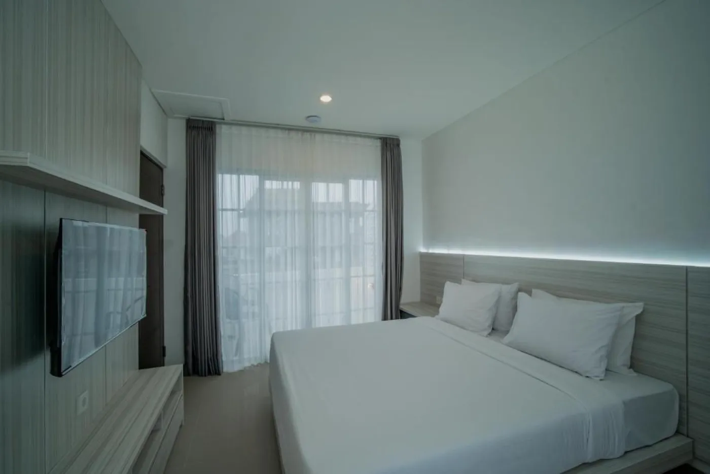 Modern minimalist living room interior with gray sofa, wooden coffee table, wall-mounted TV, built-in white shelves, and adjacent stairs. - Bali Villas