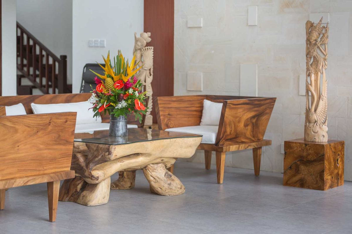 Spacious Balinese villa living room with wooden balcony, tropical furniture, stone statues, and sliding doors to lush garden. - Bali Villas