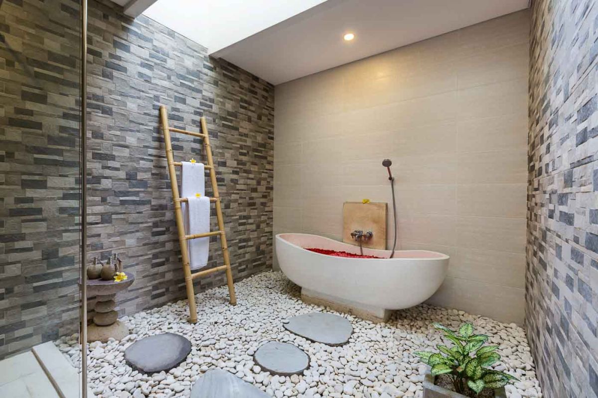 Spacious Balinese villa living room with wooden balcony, tropical furniture, stone statues, and sliding doors to lush garden. - Bali Villas