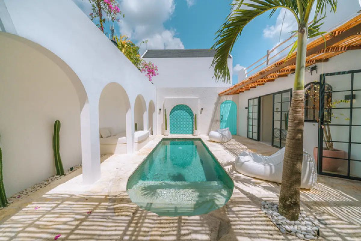 Modern tropical dining room with wooden table and chairs under a rattan pendant light, white walls, and large windows. - Bali Villas