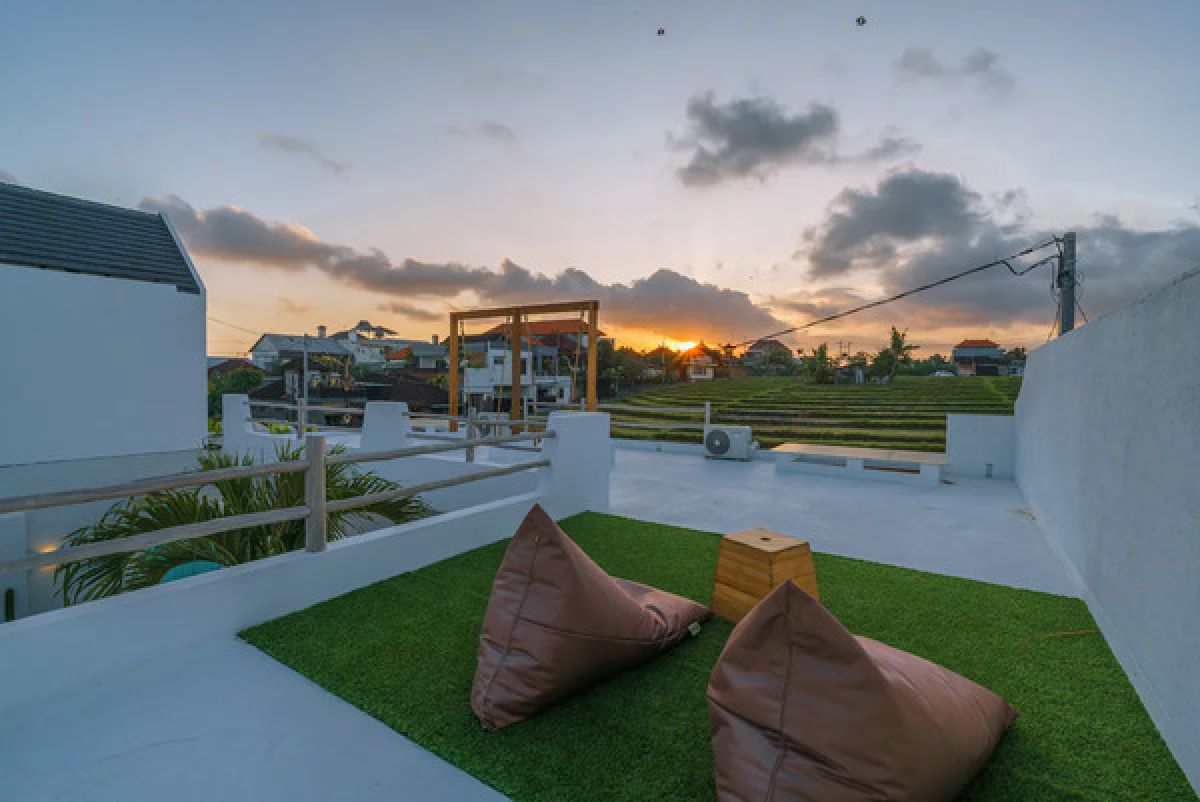 Modern tropical dining room with wooden table and chairs under a rattan pendant light, white walls, and large windows. - Bali Villas