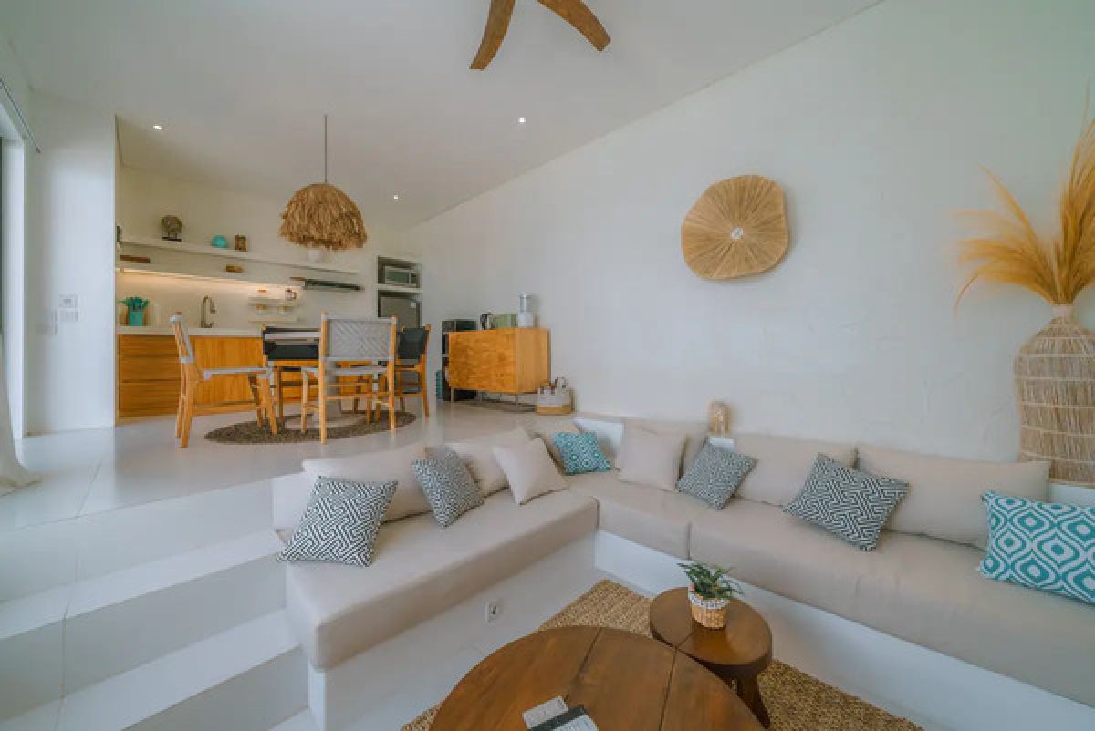 Modern tropical dining room with wooden table and chairs under a rattan pendant light, white walls, and large windows. - Bali Villas