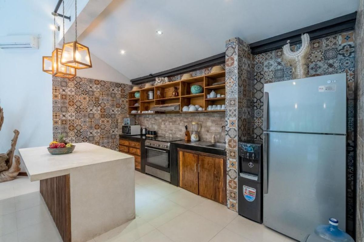 Spacious Balinese-style kitchen with intricate tiled walls, wooden cabinets, central island counter, and stainless steel appliances. - Bali Villas